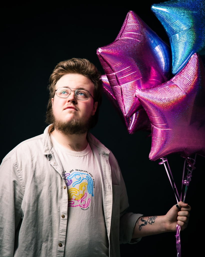 Ben Hodge holding a display of pink and blue balloons, the colours of the Trans flag