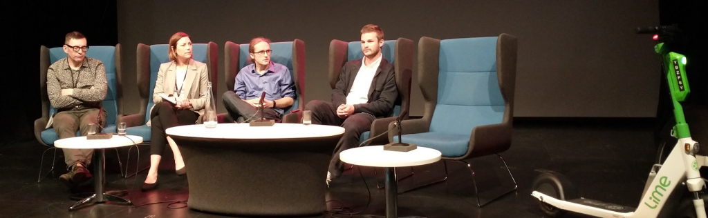 E-scooters project launch event, Media City. Panels sit in a row. E-scooter on right.