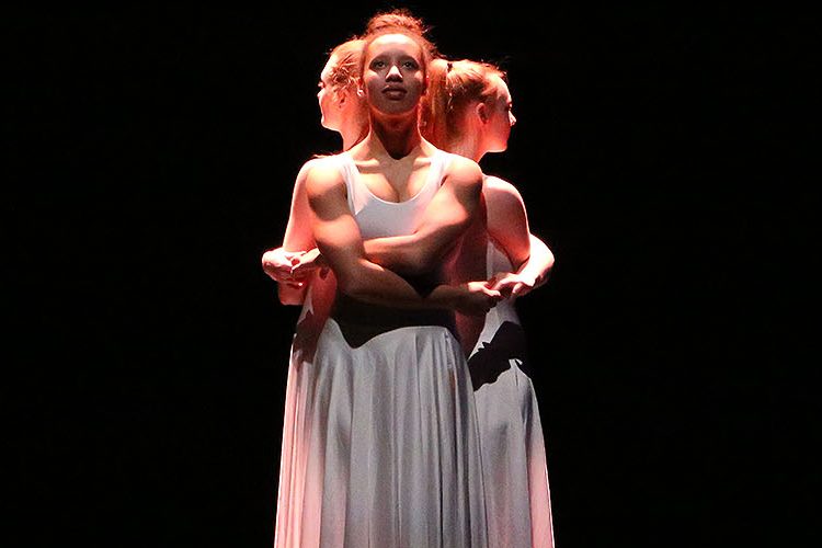 Three University of Salford students in white dresses performing on stage