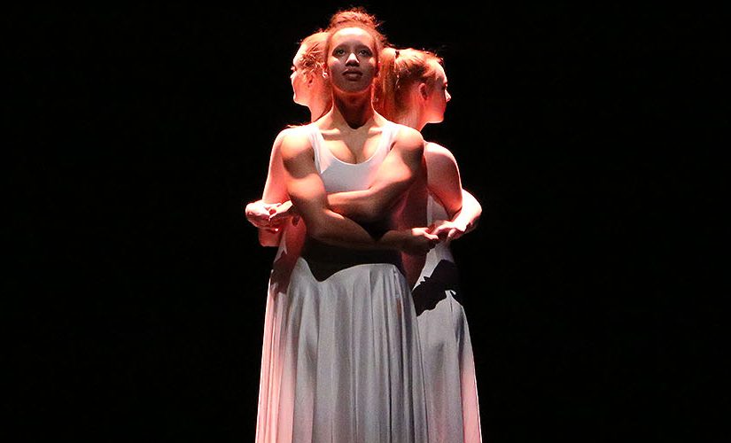 Three University of Salford students in white dresses performing on stage