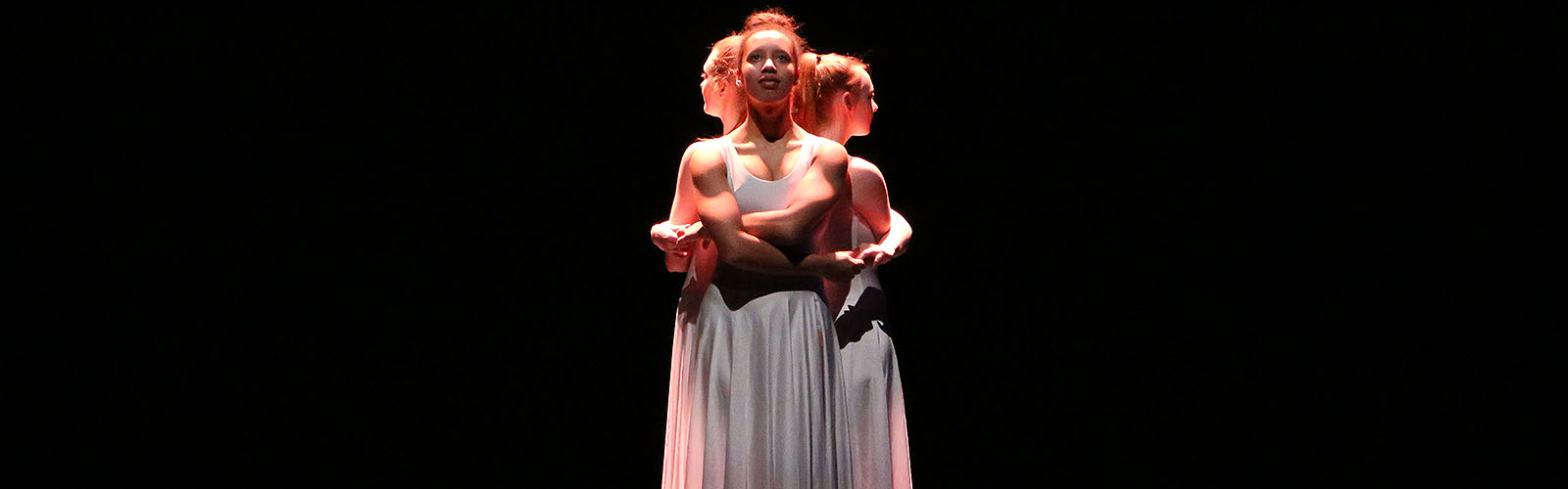 Three University of Salford students in white dresses performing on stage