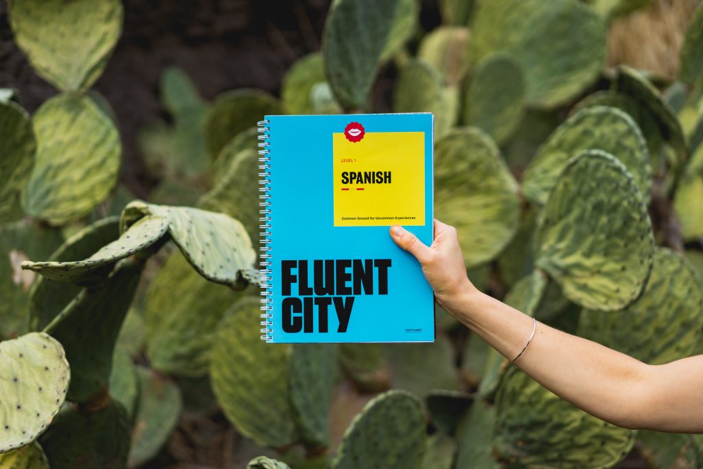 a hand holding a spanish textbook in front of cacti.