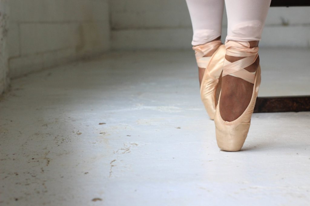 A close up of someone's feet in ballet pumps performing pointe.