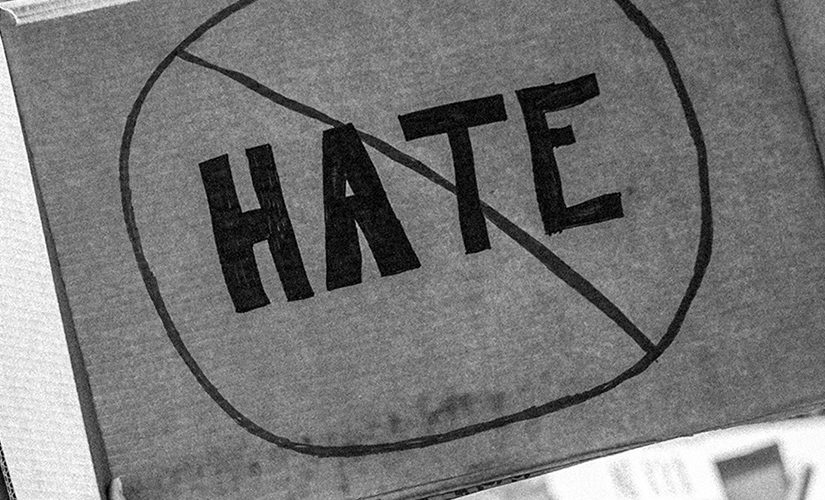 Taken or edited in black and white, someone is holding up a cardboard protest sign that shows the word 'HATE' crossed out to represent being against hate crimes