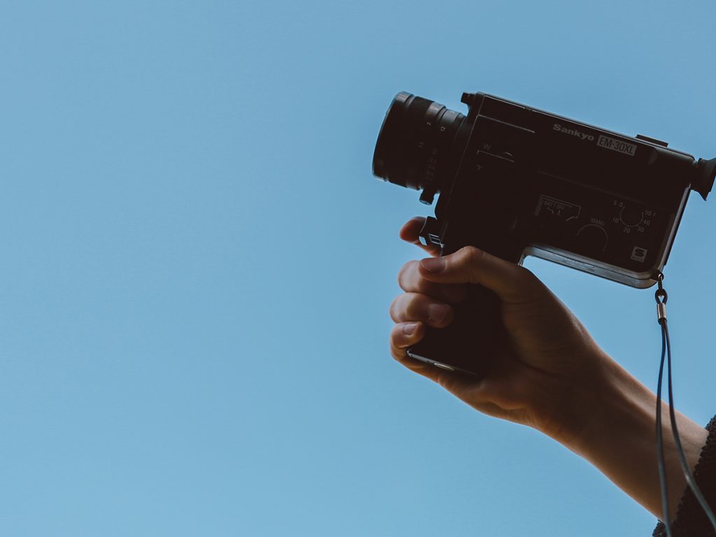 A person holds up a small Sankyo EM-30XL camera recorder with a blue sky background.