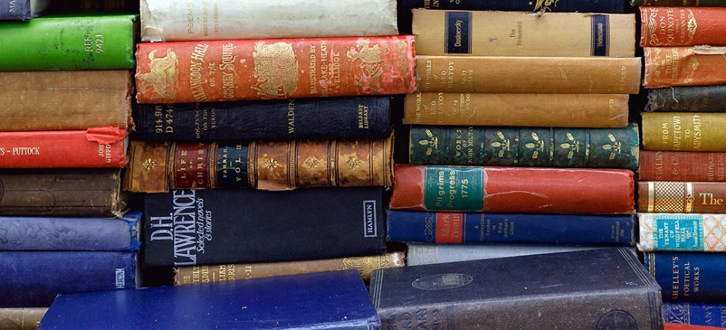 A pile of various hardback books of different colours including reds, blues, browns and green.