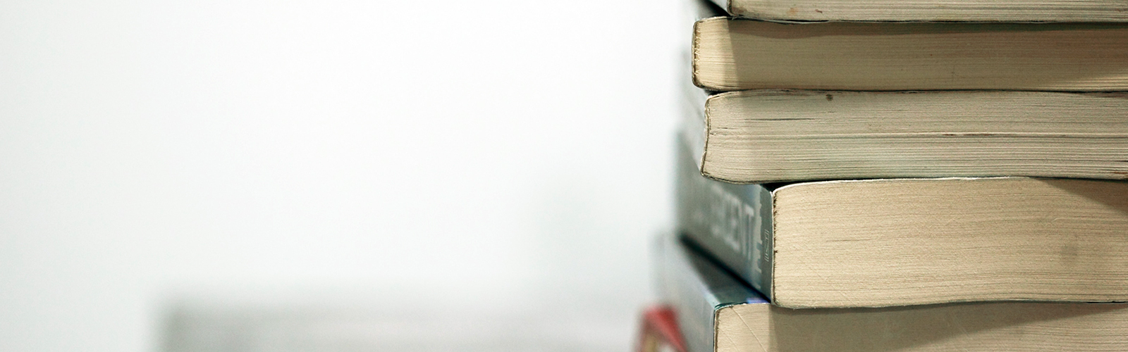 On a white background, a stack of books sits on a desk, the bottom ends of the books facing the camera.