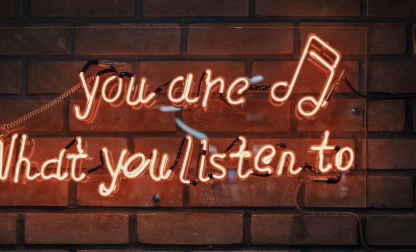 Photo of orange neon sign on a wall saying "You are, what you listen to"