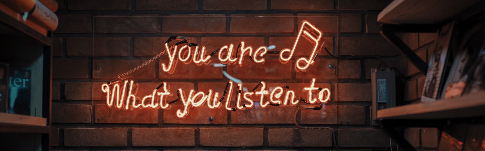 Photo of orange neon sign on a wall saying "You are, what you listen to"