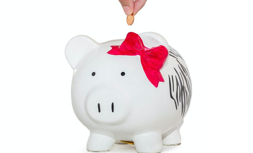 Photo of a hand putting a coin into a white piggy bank