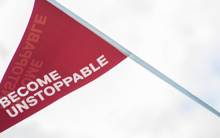 Photo of Uni of Salford tagline 'Become Unstoppable' written on a red decorative flag