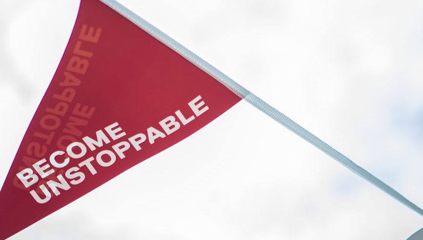 Photo of Uni of Salford tagline 'Become Unstoppable' written on a red decorative flag