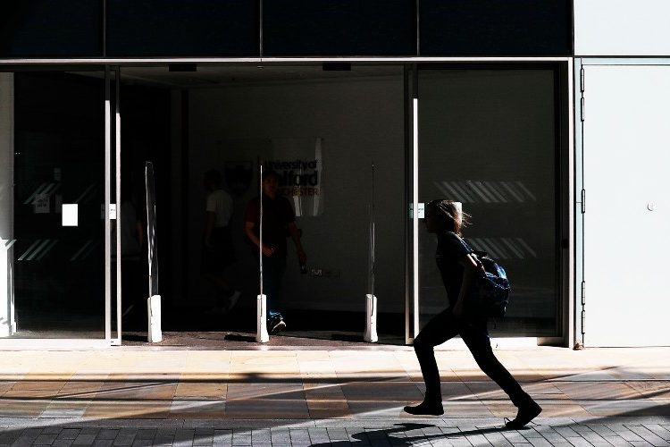 Image of the entrance to the University of Salford MCUK building, with a person walking across.