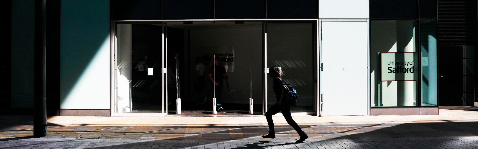 Image of the entrance to the University of Salford MCUK building, with a person walking across.