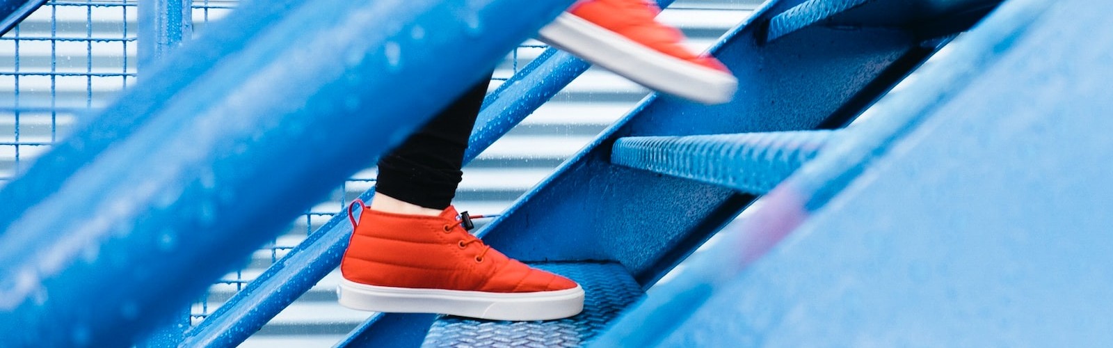 Image of a pair of feet wearing orange trainers walking up blue steps