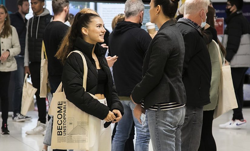 Photo of women wearing a black jacekt with a tote bag talking to counsellor wearing gray blazer