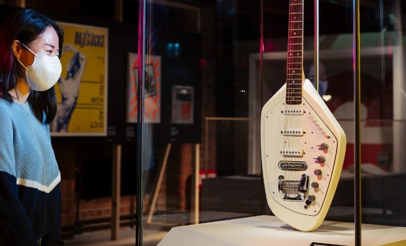 Photo of a women standing infront of a guitar that is placed is a glass box