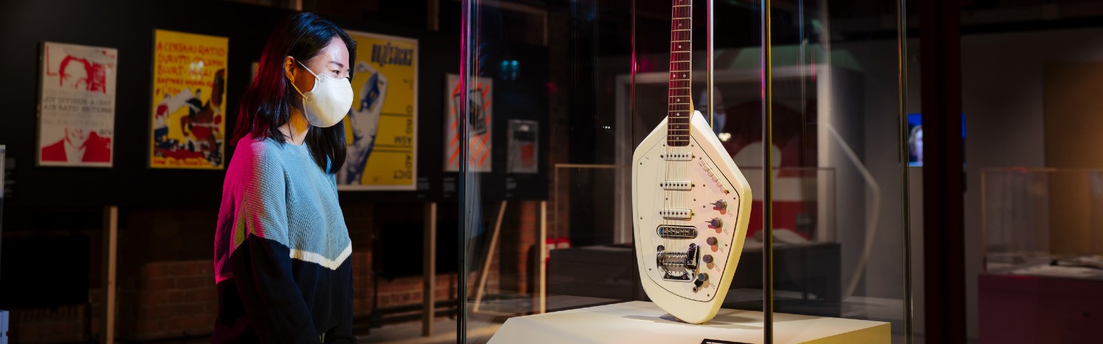 Photo of a women standing infront of a guitar that is placed is a glass box