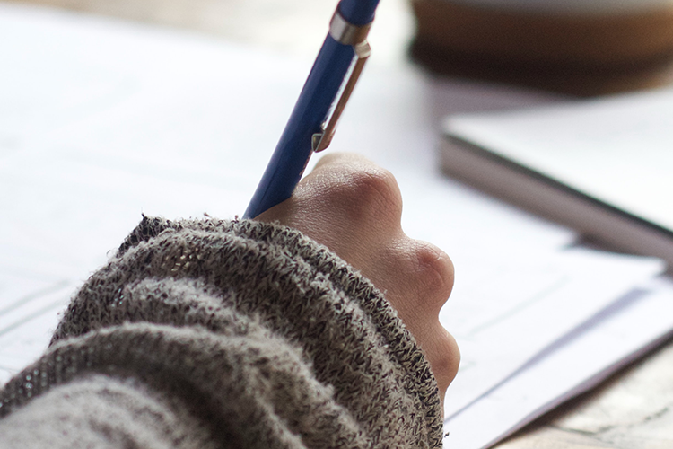 Photo of person writing on paper using a blue pen