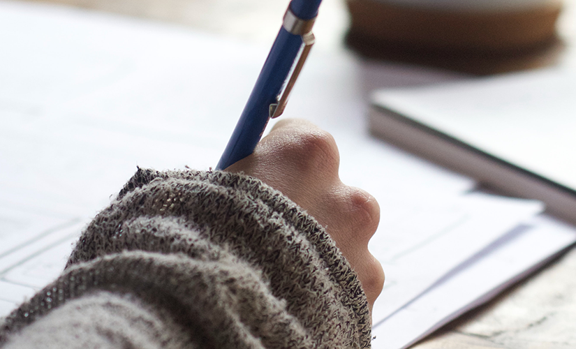 Photo of person writing on paper using a blue pen