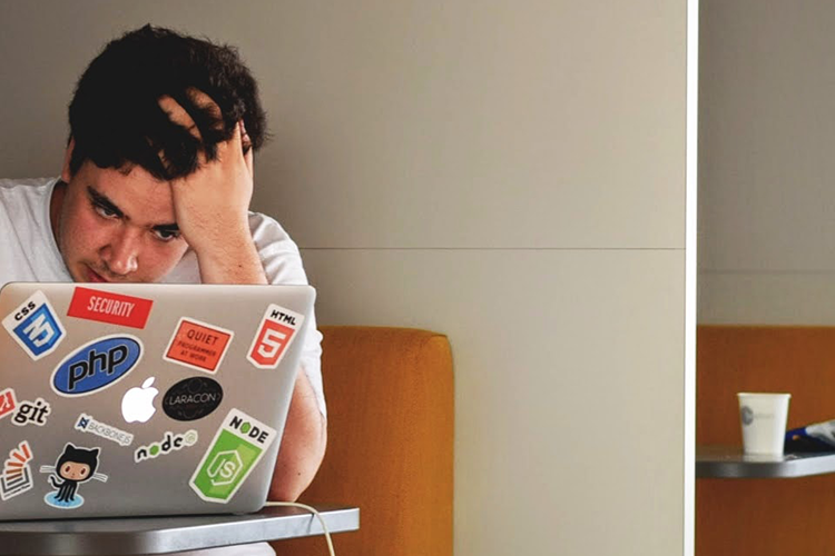 Student holding their head as they complete work on their laptop