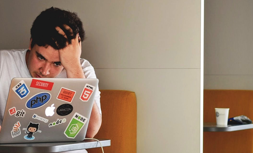 Student holding their head as they complete work on their laptop