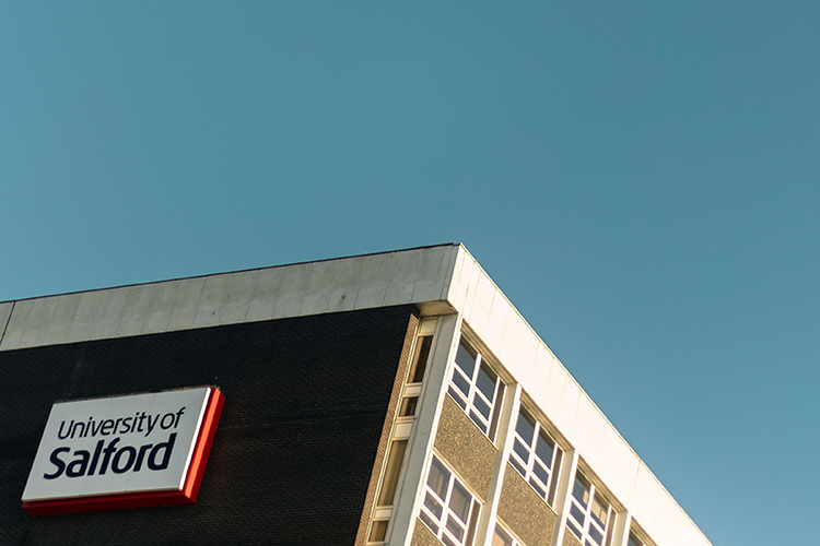 Photo of the top of a University of Salford building against a blue sky