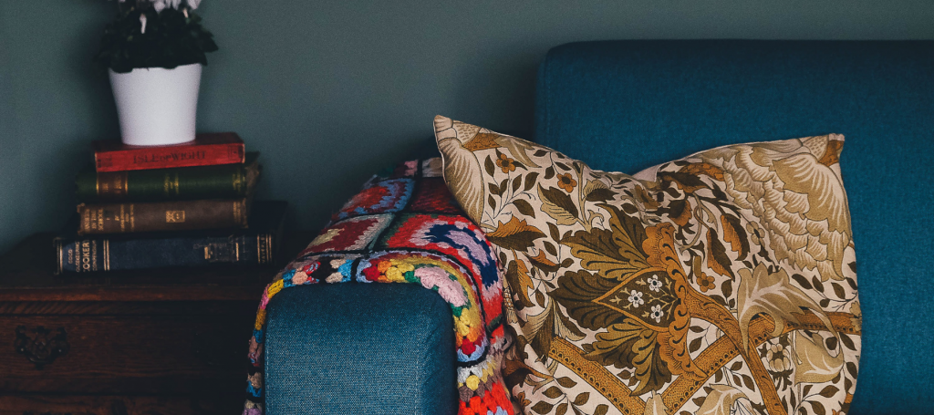 Cosy living room with a cushion and blanket on the sofa and a pile of books and plant on the coffee table.