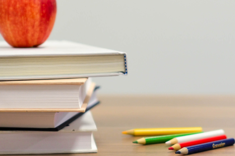 An apple placed on top of a stack of books with colored pencils and alphabet blocks to the right