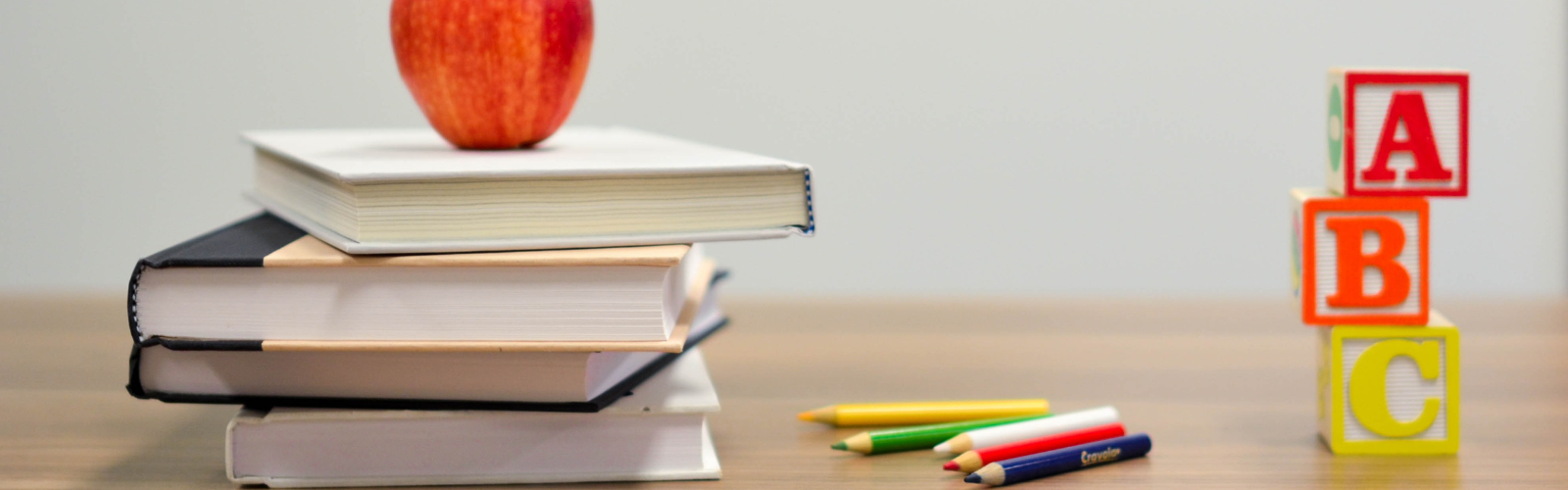 An apple placed on top of a stack of books with colored pencils and alphabet blocks to the right