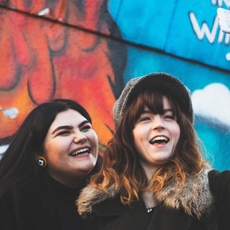 2 people taking a selfie in front of graffiti