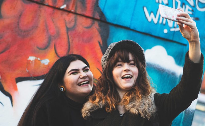 2 people taking a selfie in front of graffiti