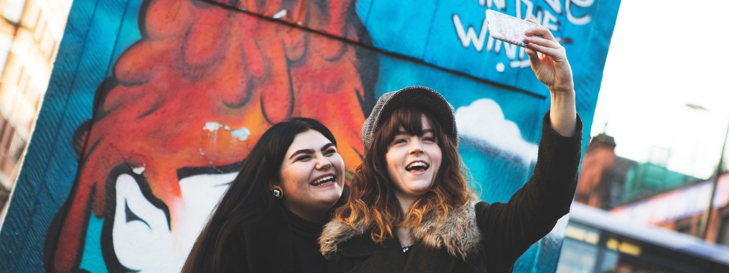 2 people taking a selfie in front of graffiti