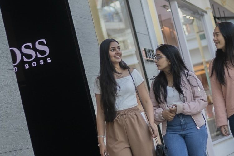 Photograph of three people walking close together in a shopping centre.