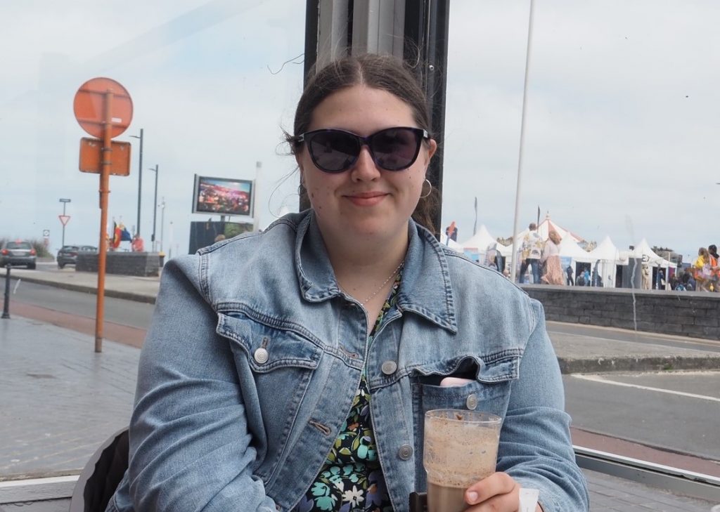 Abigail is wearing sunglasses and a denim jacket and looking at the camera