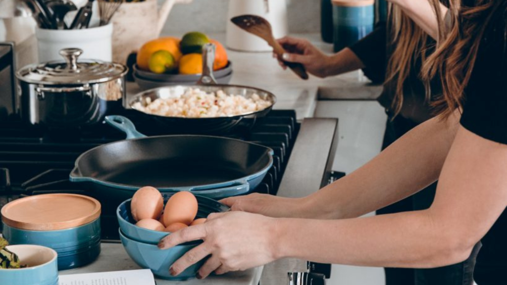 Women in the foreground holding a bowl with eggs and women in the background cooking