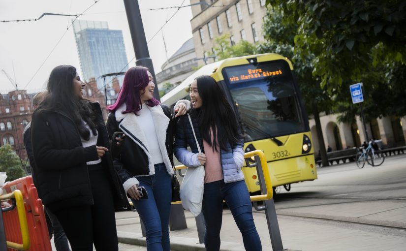 Three students walking alongside a tram